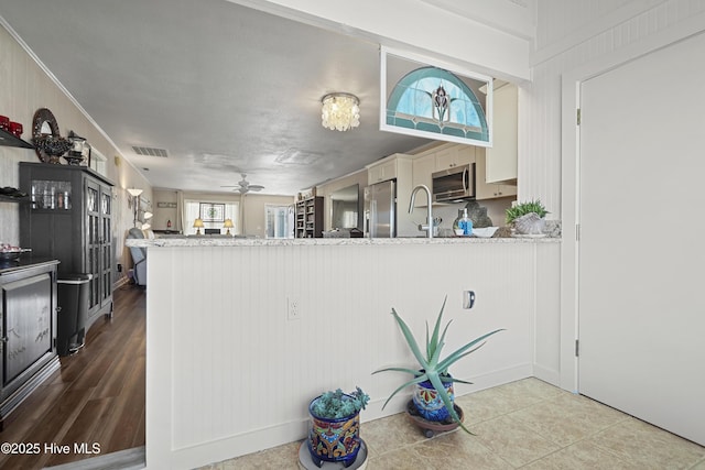 kitchen featuring stainless steel appliances, a peninsula, visible vents, a ceiling fan, and ornamental molding