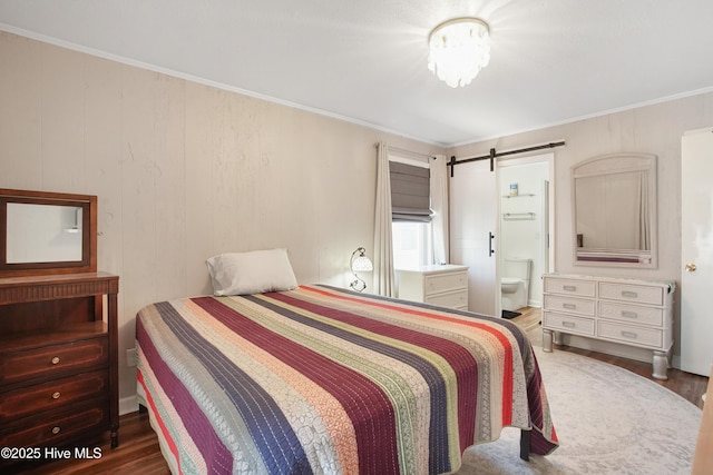 bedroom with a barn door, wood finished floors, connected bathroom, and crown molding