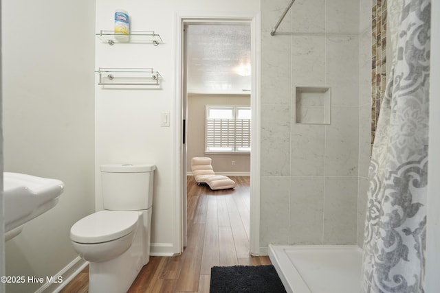 bathroom with toilet, a shower stall, baseboards, and wood finished floors