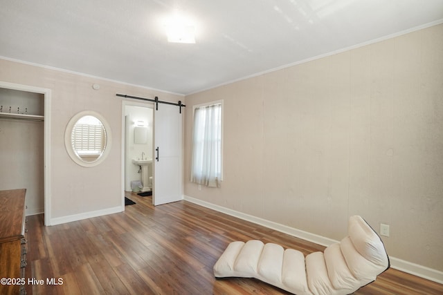 bedroom featuring ensuite bathroom, a barn door, wood finished floors, baseboards, and ornamental molding