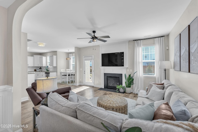 living room with baseboards, a fireplace with flush hearth, arched walkways, and light wood-style flooring