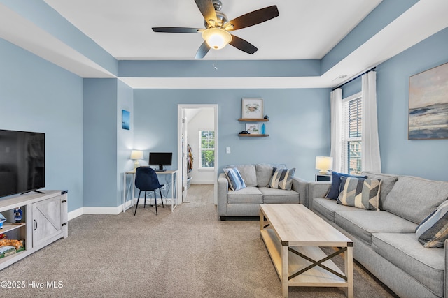 living room featuring a ceiling fan, a raised ceiling, light colored carpet, and baseboards