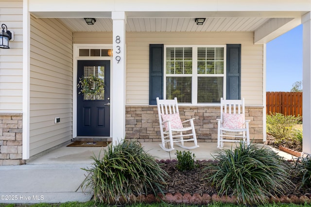 entrance to property with fence, covered porch, and stone siding