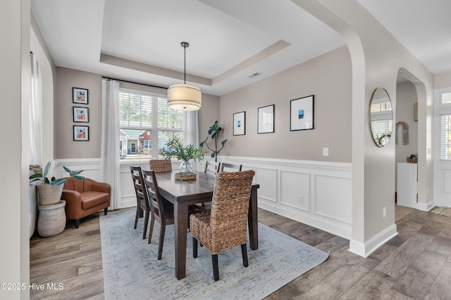 dining space with a tray ceiling, wood finished floors, arched walkways, and visible vents