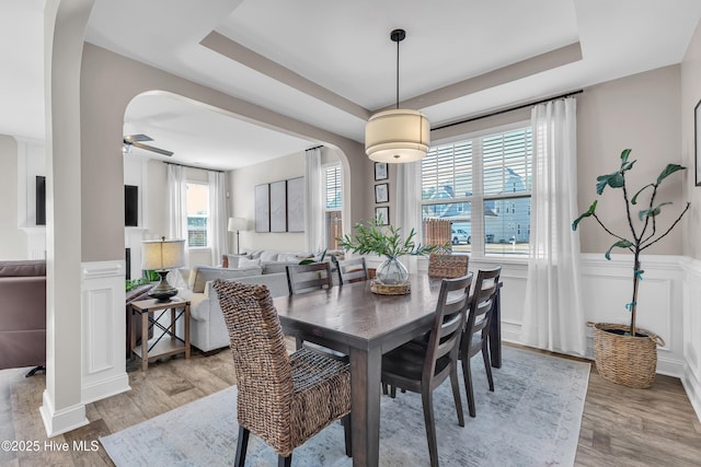 dining room featuring a tray ceiling, arched walkways, wood finished floors, and wainscoting