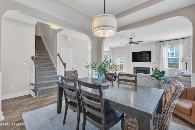 dining space with baseboards, stairs, wood finished floors, arched walkways, and a glass covered fireplace