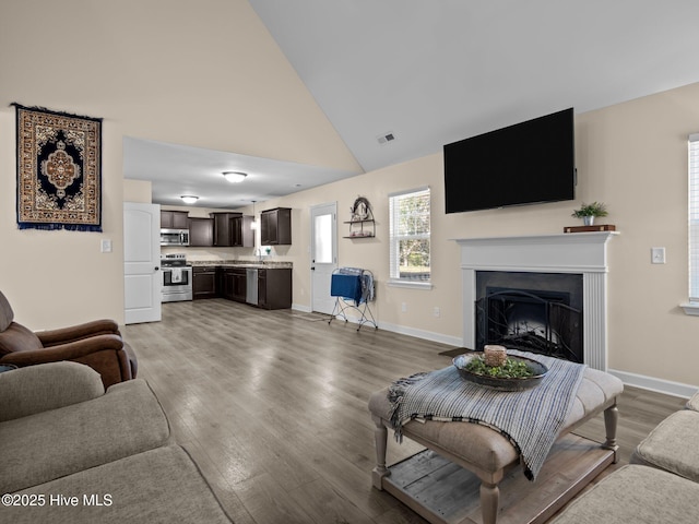 living room featuring light wood finished floors, a fireplace, baseboards, and high vaulted ceiling