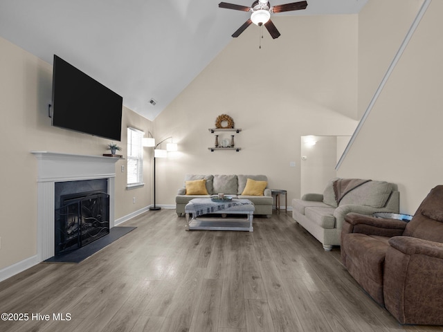 living room featuring a fireplace with raised hearth, high vaulted ceiling, wood finished floors, and baseboards