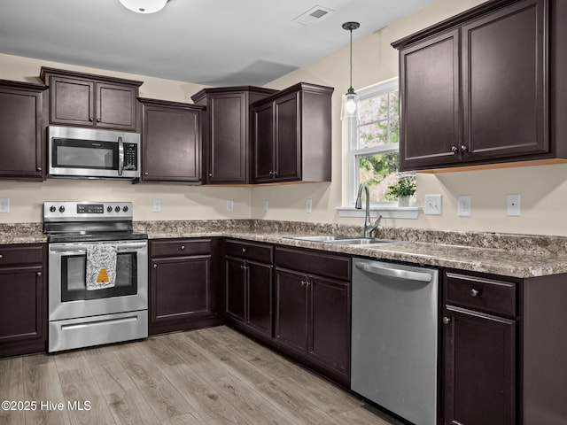 kitchen with stainless steel appliances, a sink, dark brown cabinetry, and light wood-style floors