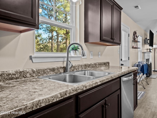 kitchen with dark brown cabinetry, visible vents, light wood-style flooring, a sink, and stainless steel dishwasher