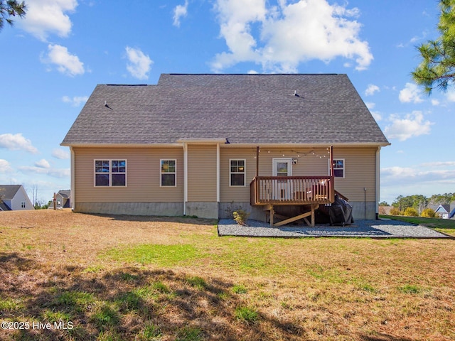 back of property featuring a shingled roof, a deck, and a lawn