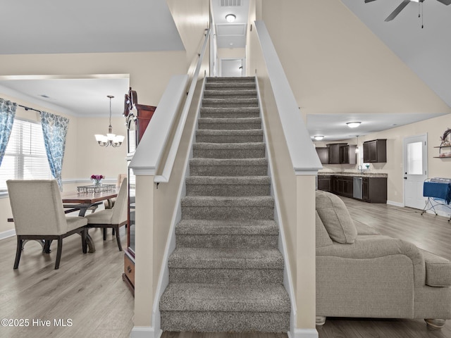 stairway with ceiling fan with notable chandelier, wood finished floors, and baseboards