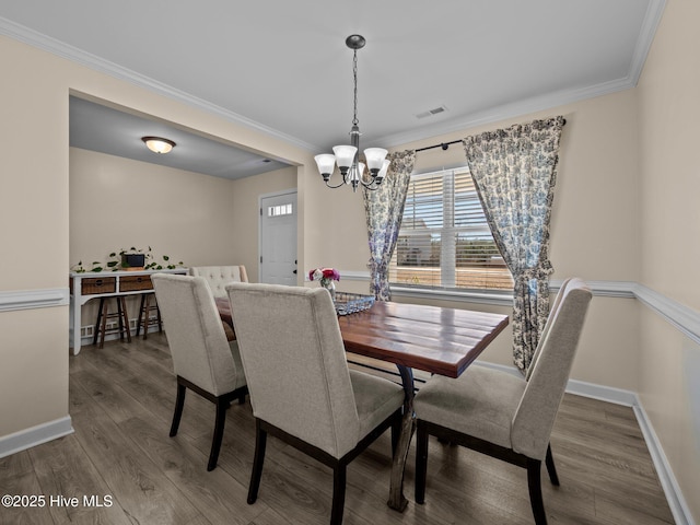 dining space featuring baseboards, visible vents, wood finished floors, crown molding, and a notable chandelier