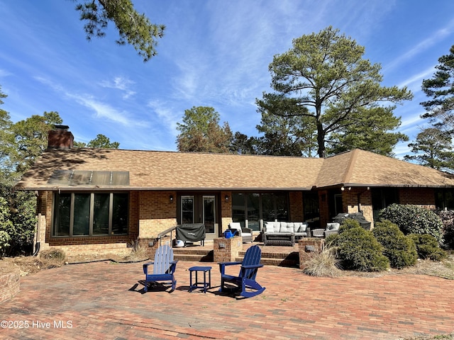 back of house featuring brick siding, a chimney, outdoor lounge area, and roof with shingles