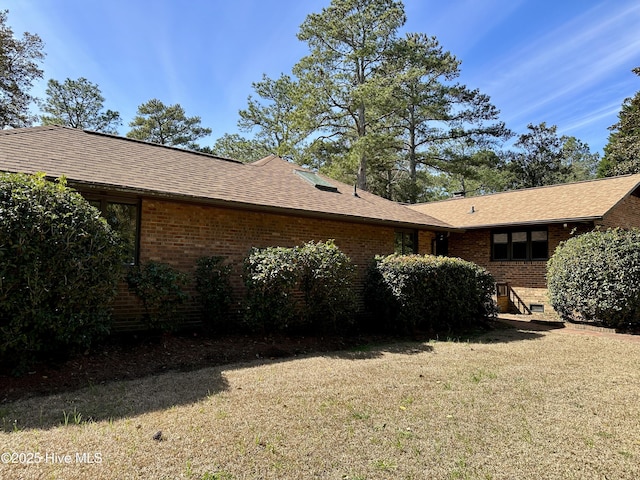 view of side of property featuring a shingled roof, brick siding, and a lawn