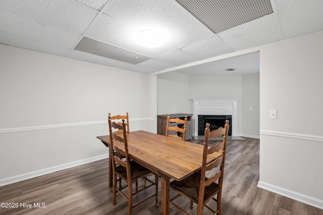 dining space with a fireplace with flush hearth, visible vents, baseboards, and wood finished floors