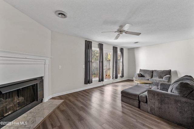 living room featuring a textured ceiling, a fireplace, wood finished floors, a ceiling fan, and baseboards