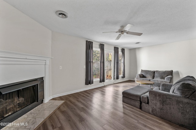 living room with a textured ceiling, baseboards, a ceiling fan, wood finished floors, and a tile fireplace
