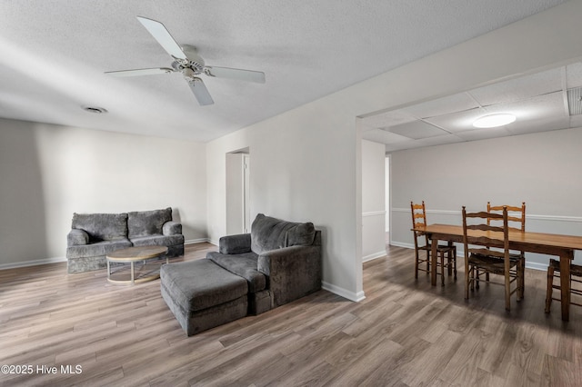 living area with baseboards, a ceiling fan, wood finished floors, and visible vents