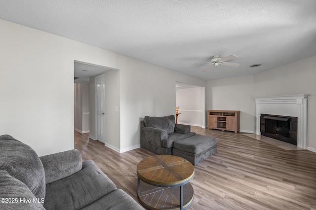 living area with a fireplace with flush hearth, wood finished floors, baseboards, a textured ceiling, and ceiling fan