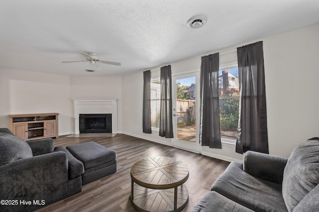 living area featuring a fireplace with flush hearth, a textured ceiling, baseboards, and wood finished floors