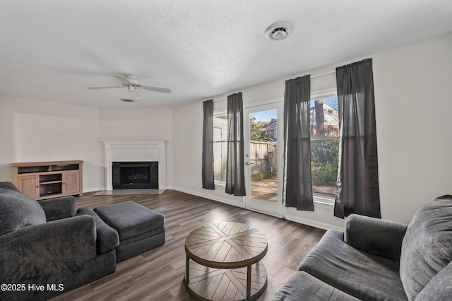 living room featuring a fireplace with flush hearth, a textured ceiling, baseboards, wood finished floors, and ceiling fan