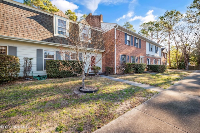 view of front of property with brick siding, a shingled roof, a chimney, and a front yard