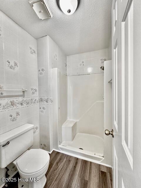 bathroom featuring a textured ceiling, toilet, tile walls, a stall shower, and wood finished floors