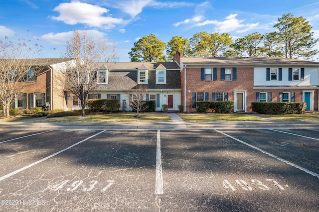 view of front of house featuring uncovered parking, a chimney, and brick siding