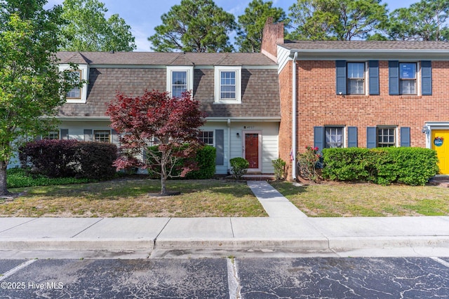 view of front facade featuring a chimney, a front lawn, brick siding, and a shingled roof