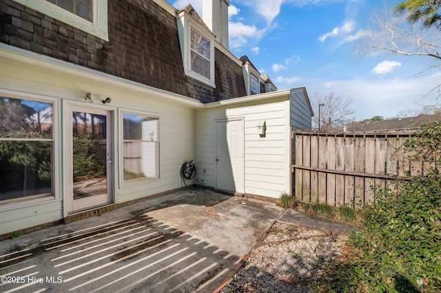 rear view of property featuring a patio area, fence, mansard roof, and roof with shingles