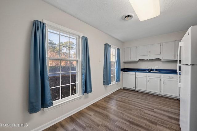 kitchen featuring white appliances, baseboards, dark wood finished floors, dark countertops, and a sink