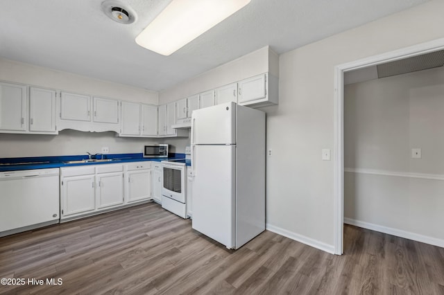 kitchen with wood finished floors, a sink, white appliances, white cabinetry, and under cabinet range hood