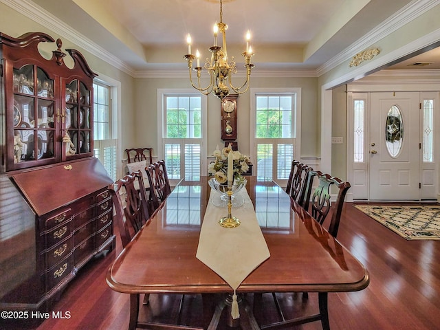 dining area with an inviting chandelier, a tray ceiling, wood finished floors, and ornamental molding