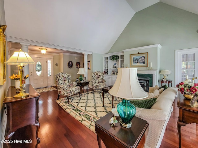 living area with high vaulted ceiling, a glass covered fireplace, wood finished floors, and built in shelves