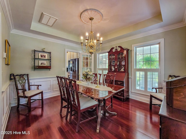 dining area with a decorative wall, a wainscoted wall, a notable chandelier, dark wood-style flooring, and a tray ceiling