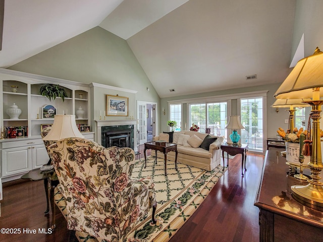 living room featuring high vaulted ceiling, dark wood-style flooring, a glass covered fireplace, and visible vents