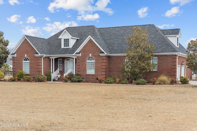 view of front facade with brick siding, a front yard, and a shingled roof