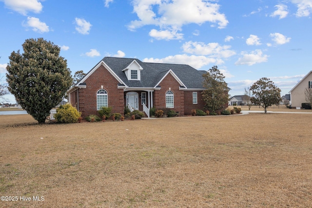 view of front facade with a front yard, brick siding, and roof with shingles