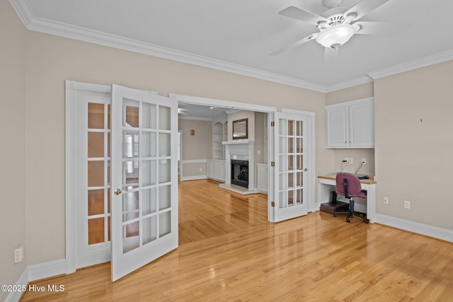 unfurnished office featuring a fireplace with raised hearth, french doors, light wood-style flooring, and a ceiling fan