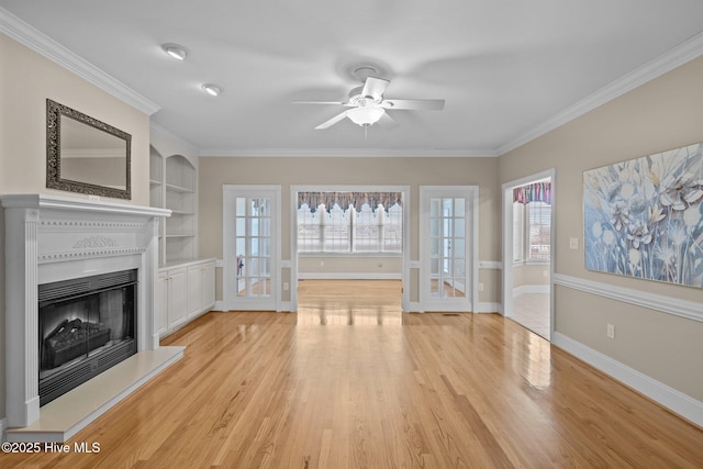 unfurnished living room featuring baseboards, a fireplace with raised hearth, ornamental molding, light wood-type flooring, and built in shelves