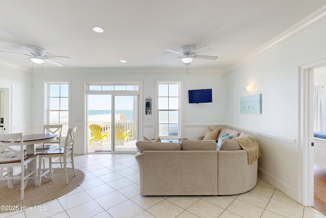 living room featuring light tile patterned floors, ornamental molding, wainscoting, and a ceiling fan