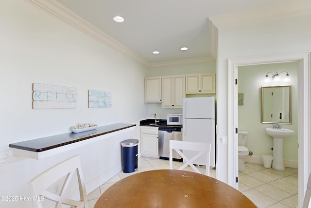 kitchen with a sink, white appliances, light tile patterned floors, and cream cabinetry