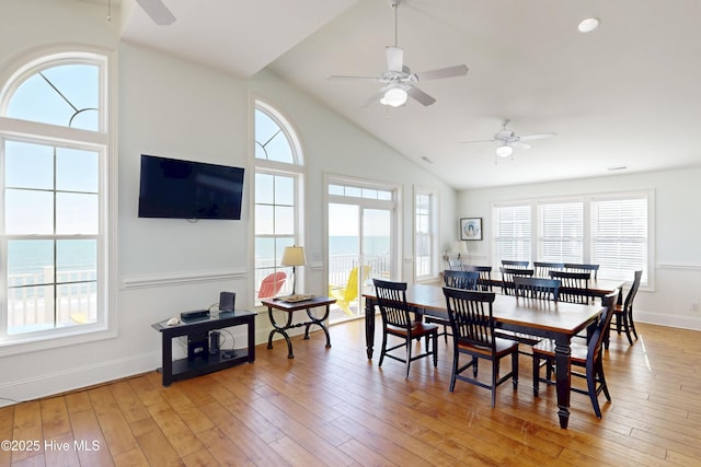 dining space featuring baseboards, high vaulted ceiling, light wood-type flooring, and a healthy amount of sunlight