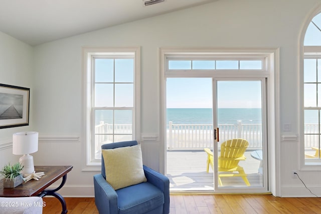 sitting room featuring lofted ceiling, a water view, light wood-style flooring, and visible vents