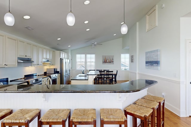 kitchen featuring stainless steel appliances, a wainscoted wall, under cabinet range hood, and light wood finished floors