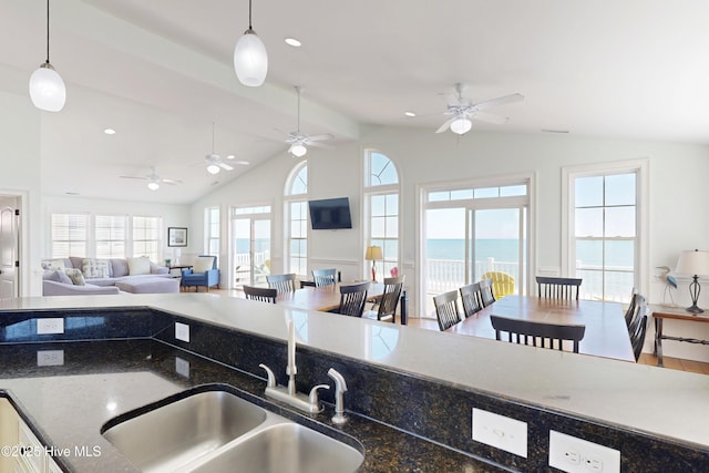 kitchen with lofted ceiling, dark stone countertops, pendant lighting, and a sink