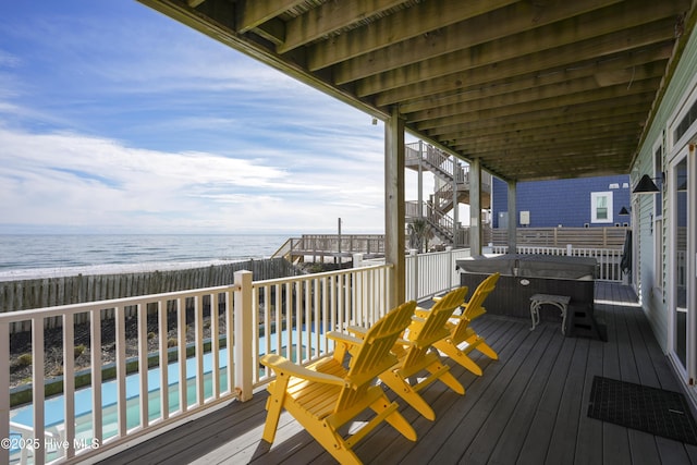 wooden deck with a swimming pool, a water view, fence, and a view of the beach