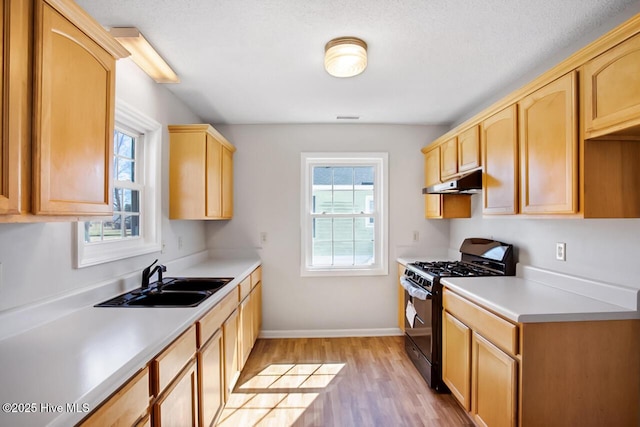 kitchen featuring black gas range, light wood finished floors, light brown cabinetry, under cabinet range hood, and a sink