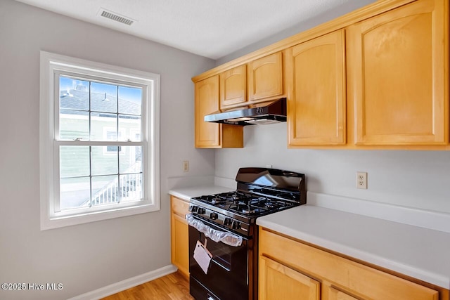 kitchen with under cabinet range hood, visible vents, black gas stove, light countertops, and light brown cabinetry